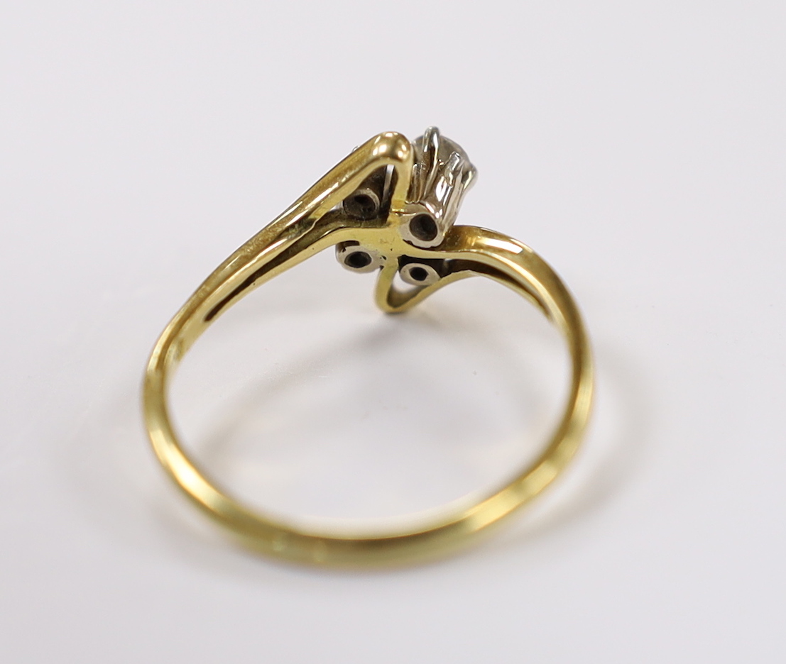 A yellow metal and graduated four stone diamond set crossover ring, size R, gross weight 3.4 grams.
